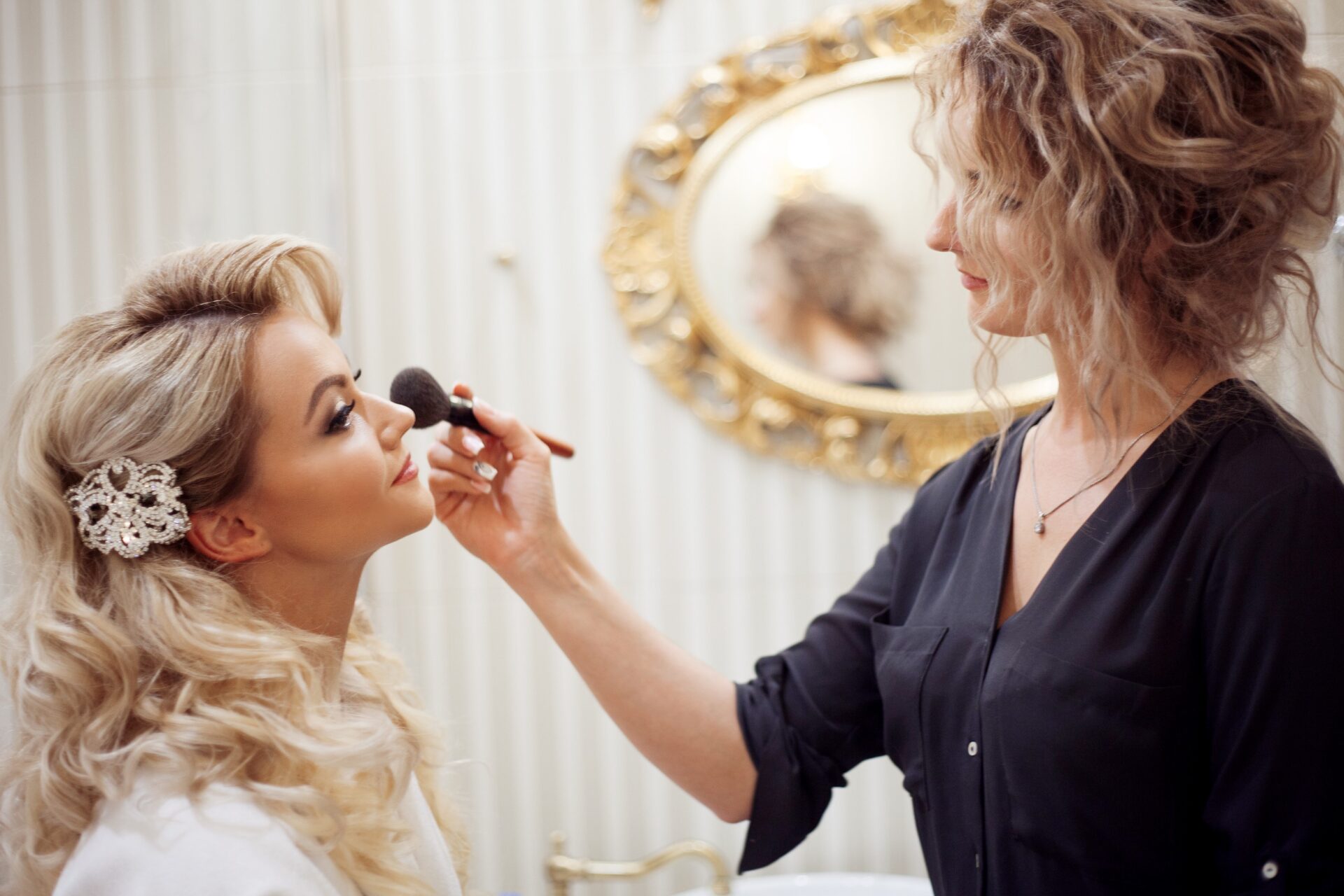 In a mirror reflection, a woman expertly applies makeup to a bride